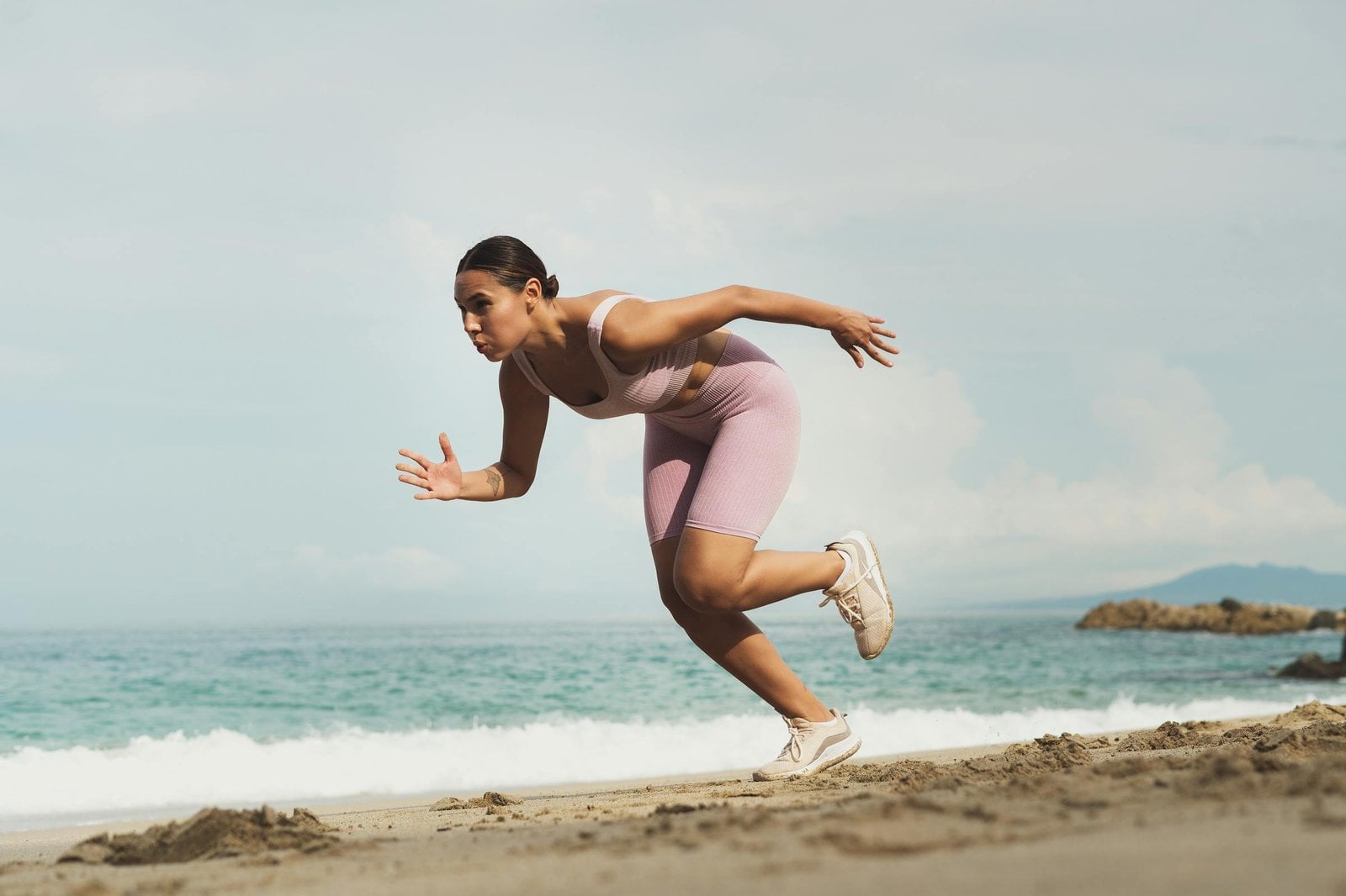 Mulher brasileira correndo na praia, em plano aproximado, focada no movimento — atividade física como parte do plano de emagrecimento com acompanhamento médico.